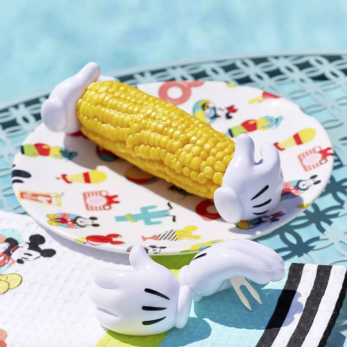 two corn holders attached to both ends of an ear of corn on a plate and two additional holders sitting beside the plate