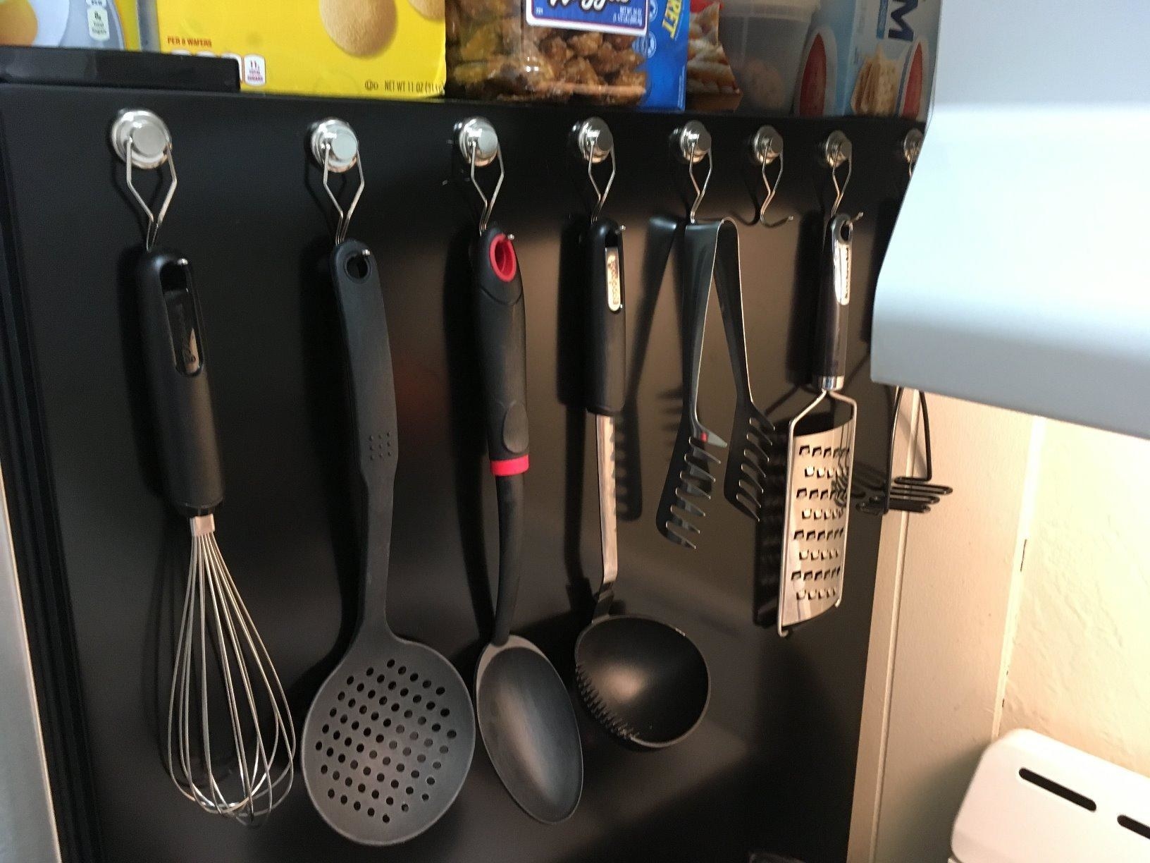 Eight silver magnetic hooks attached to a refrigerator holding utensils