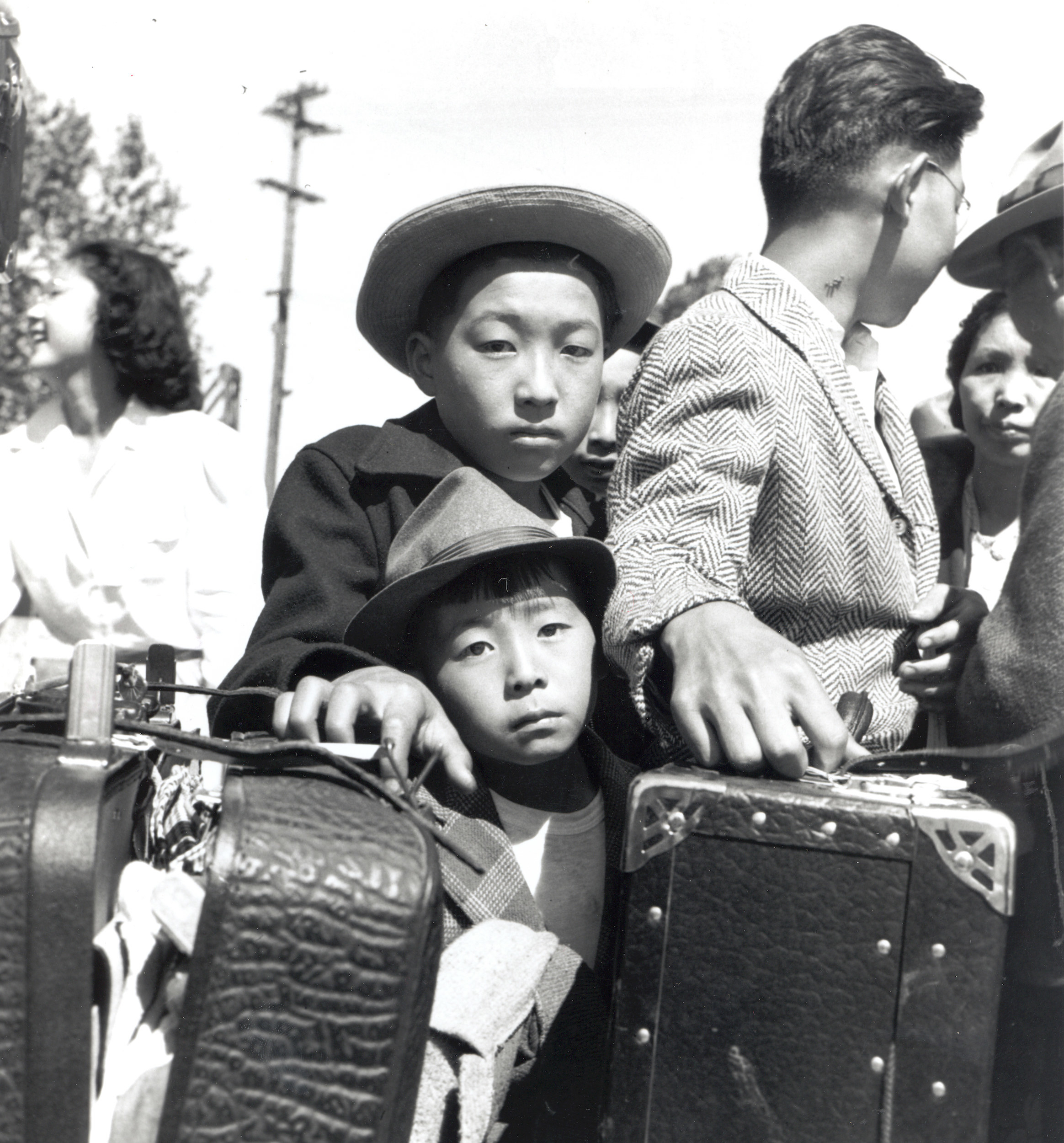 Two young Japanese boys with their family and suitcases are waiting for baggage inspections at an internment camp