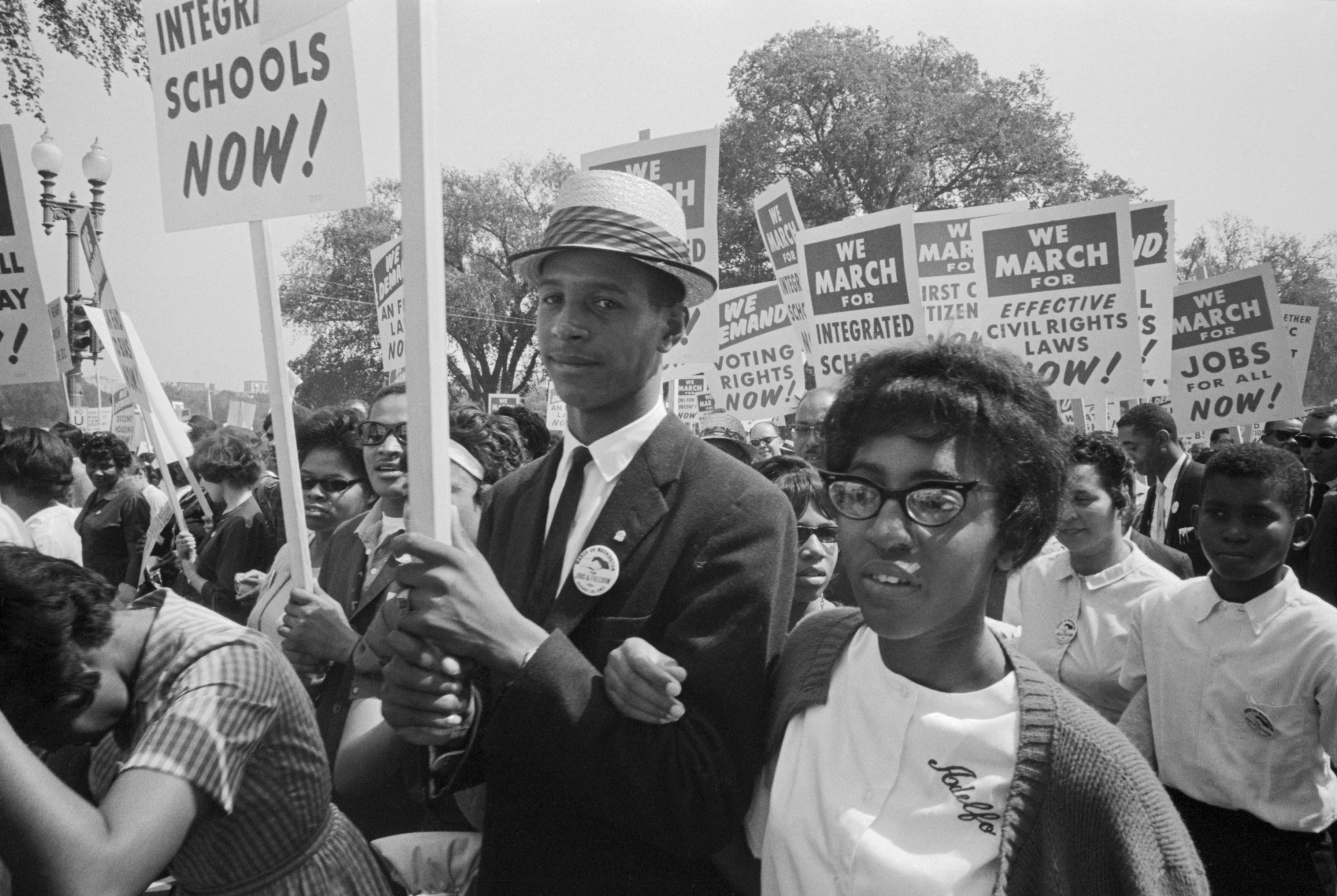 A young Black girl and boy marching with Black students, holding signs that call for integrated schools, voting rights, jobs, and civil rights 