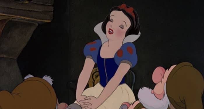 Snow White sitting on a chair in the cottage and singing to the dwarfs