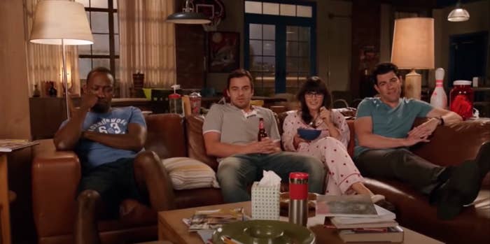 The roommates on "New Girl" sit on the couch together and watch TV.