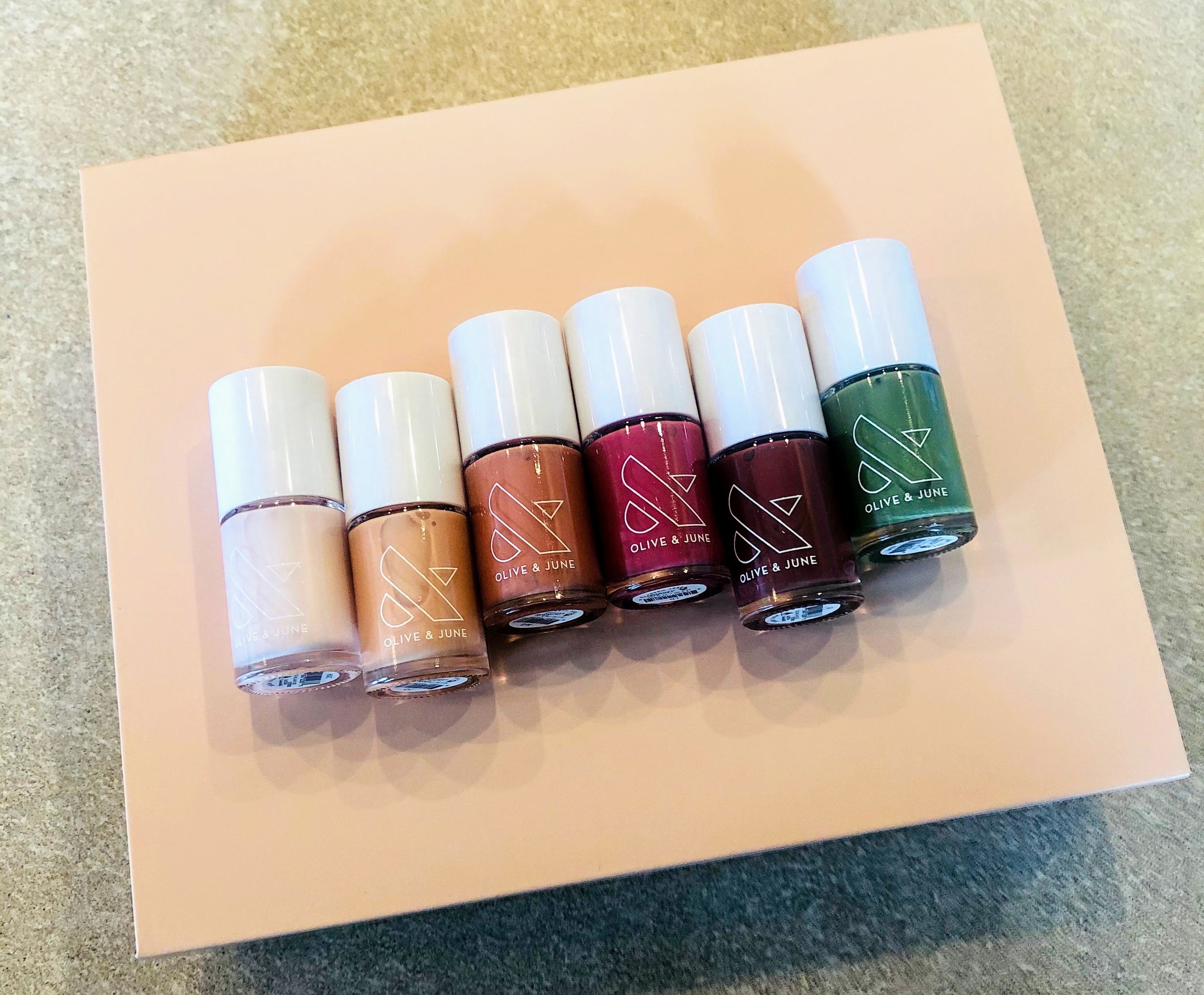 A cream box with six nail polish bottle on top in cream, yellow, orange, red, brown, and green. 