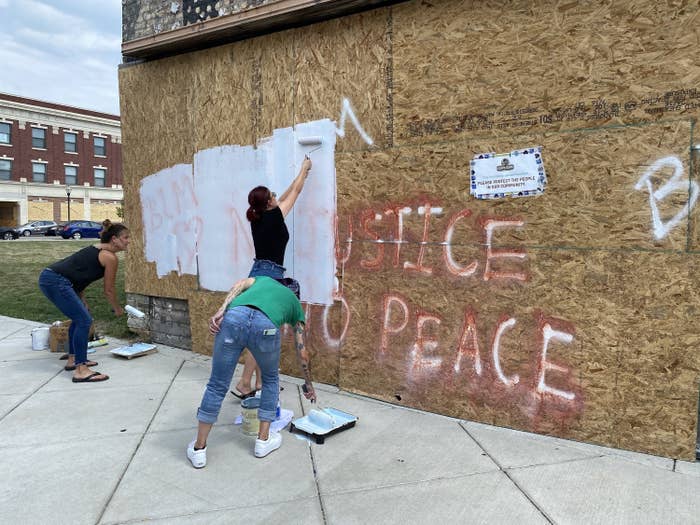 People paint white over a wall that says "No justice, no peace"