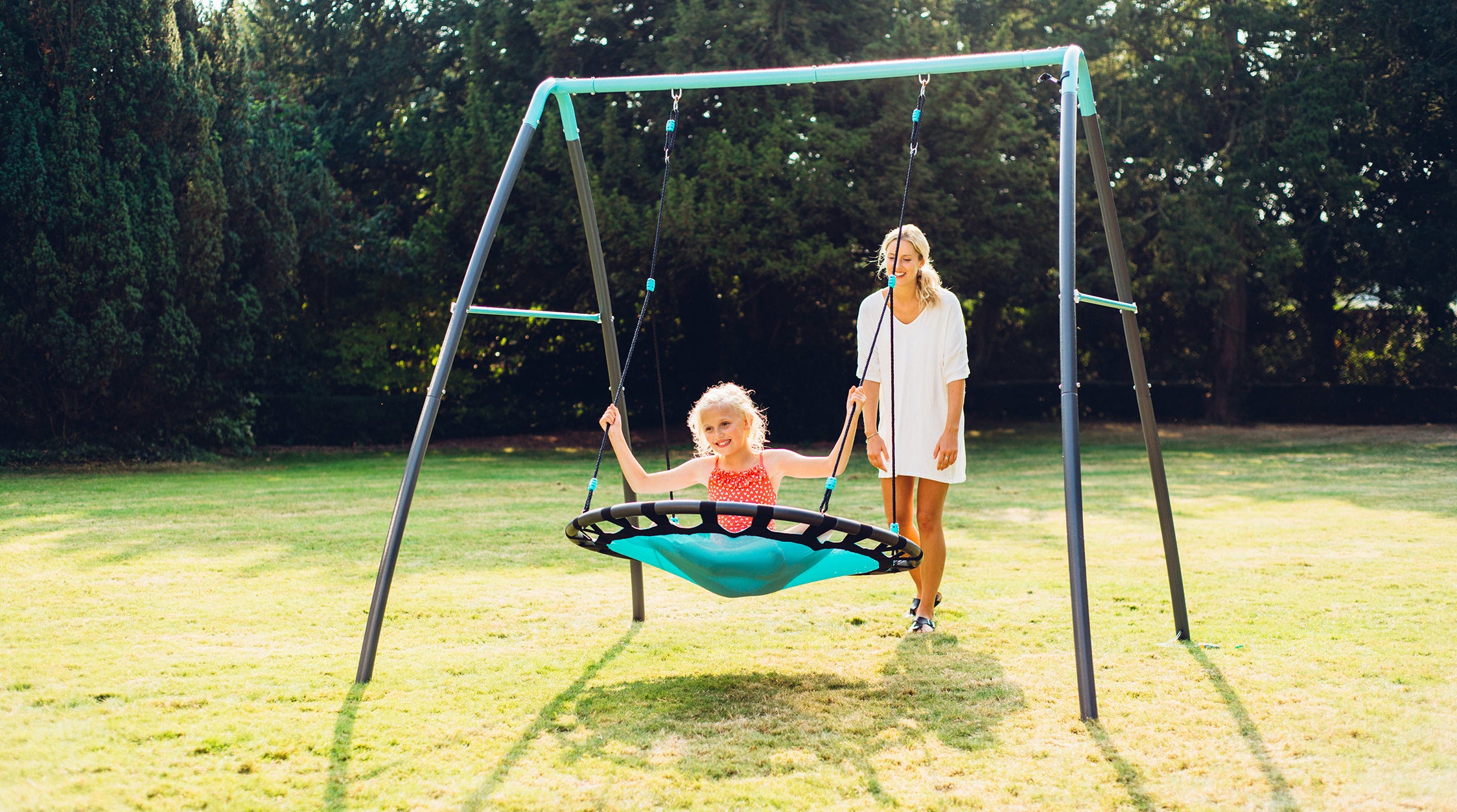 a mother pushing a girl in a metal nest swing
