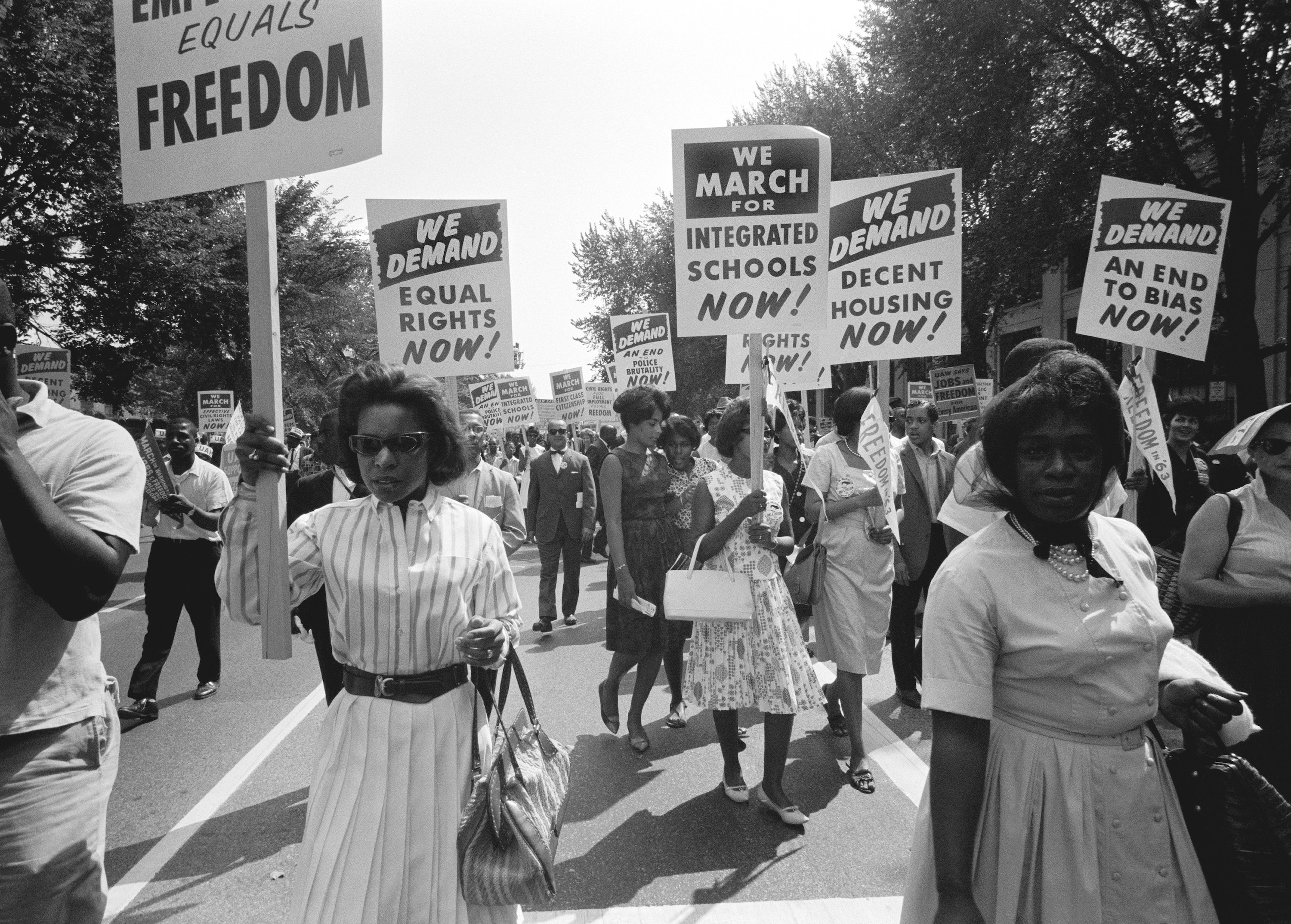 Black women marching in the March on Washington with signs that say, &quot;We march for integrated schools nows,&quot; &quot;We demand equal rights now,&quot; &quot;We demand decent housing now,&quot; and &quot;We demand an end to bias now.&quot;