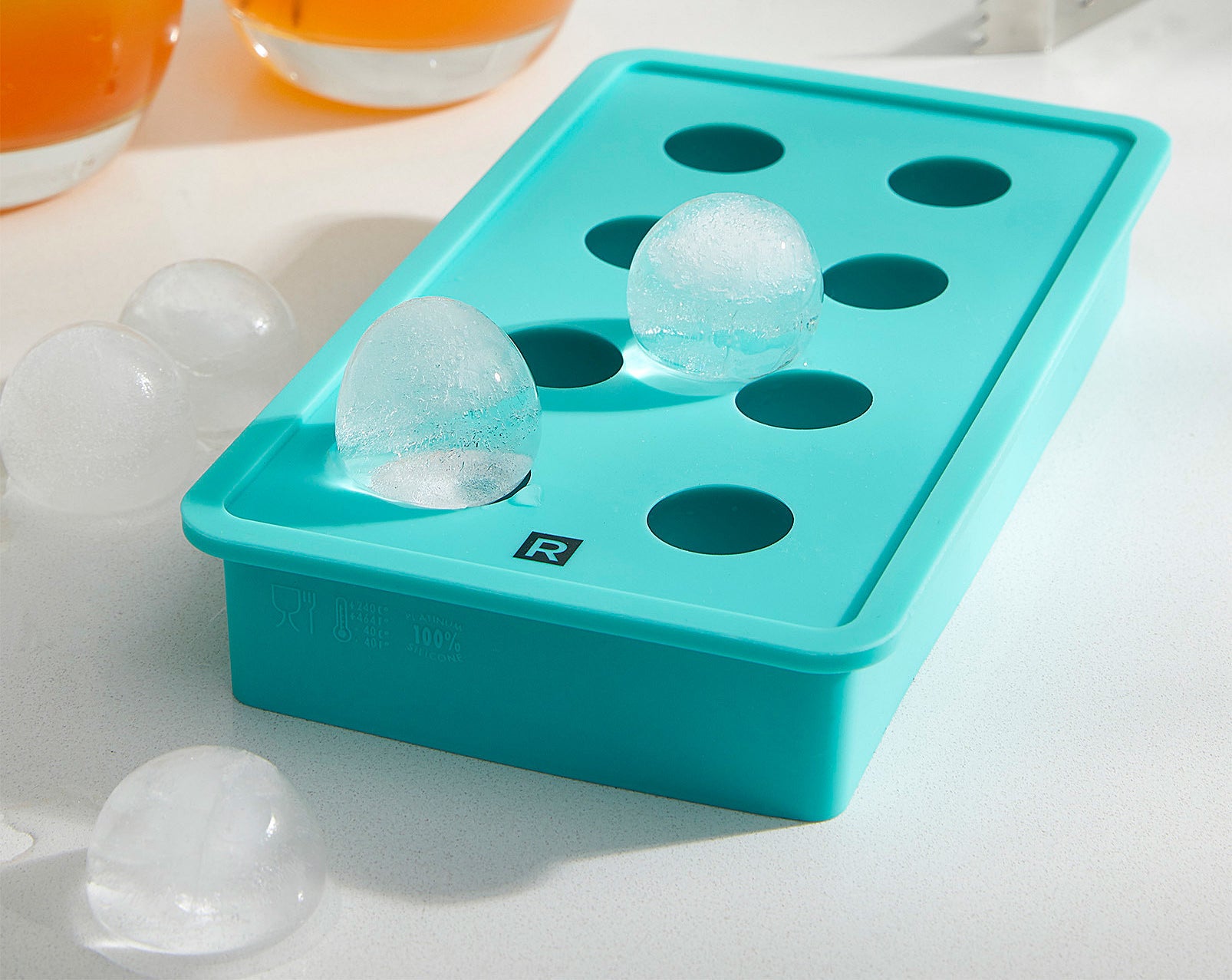 A silicone ice cube tray with round blocks of ice on top and beside it