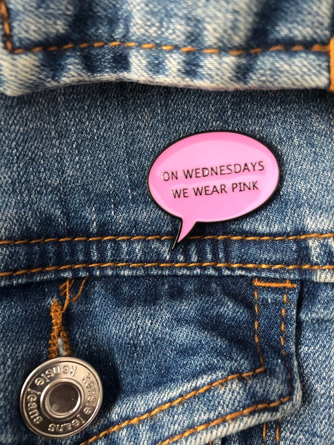A small pin on a jean jacket that says on Wednesdays we wear pink