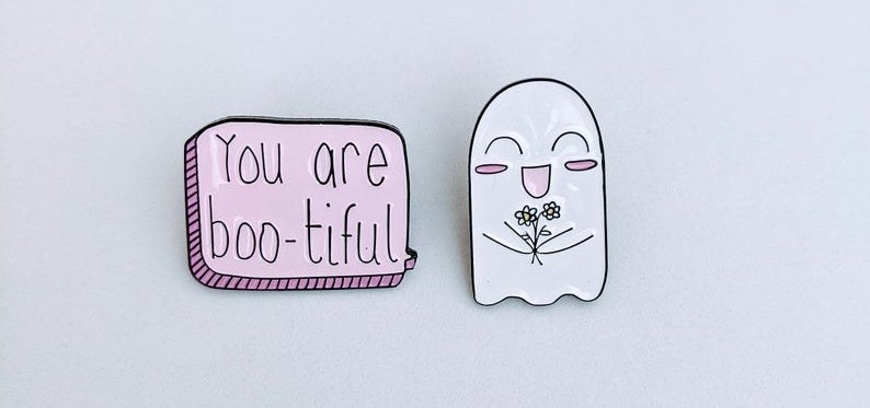 A pin with a happy looking ghost holding flowers and a pin that says you are boo-toful