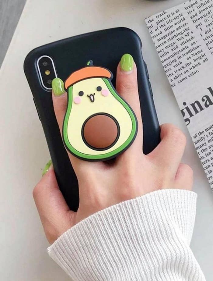 A pop socket with a happy looking avocado on the back of a phone
