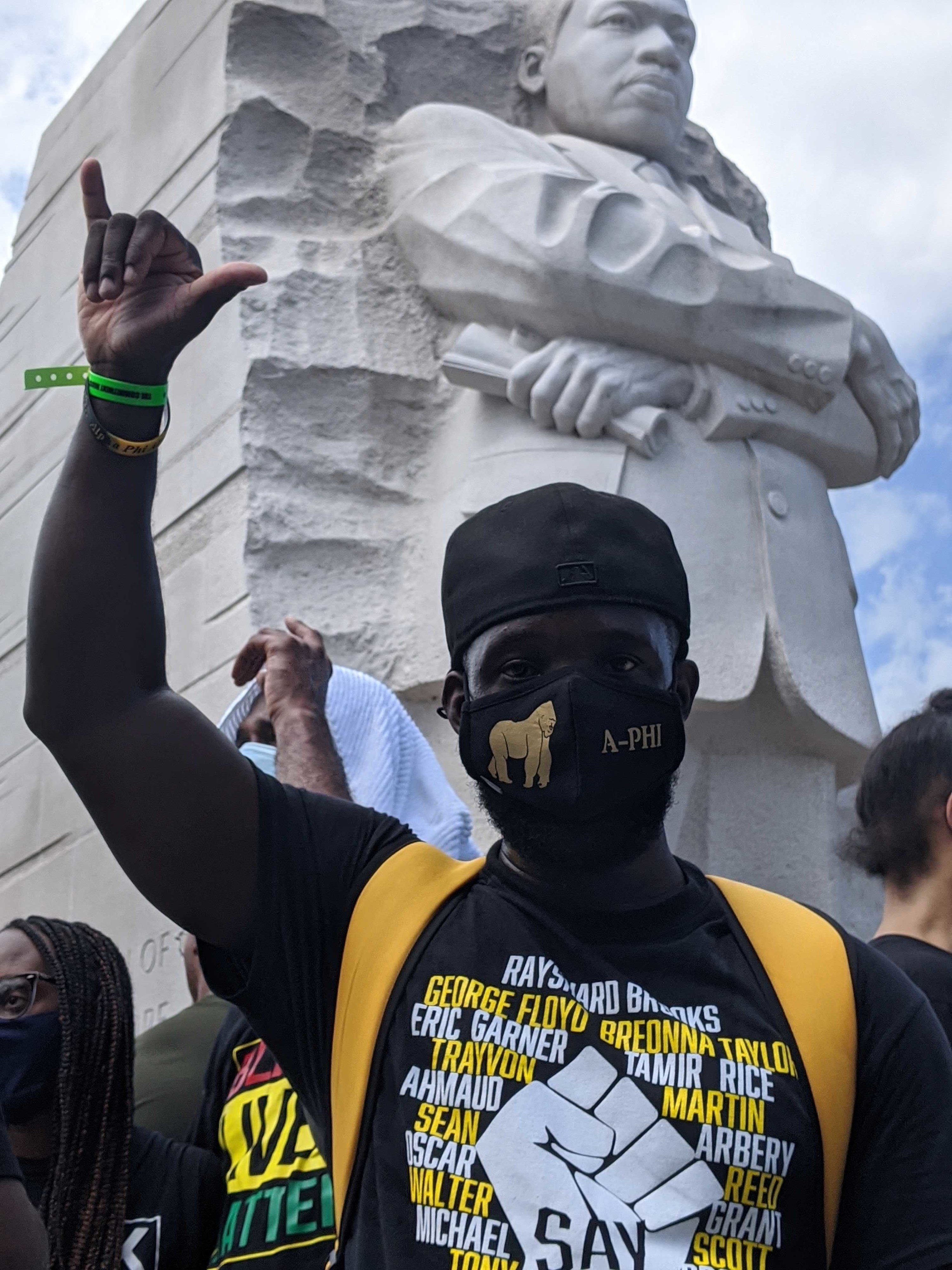 A man stands giving a hang loose sign with his hand in front of the Martin Luther King Jr memorial