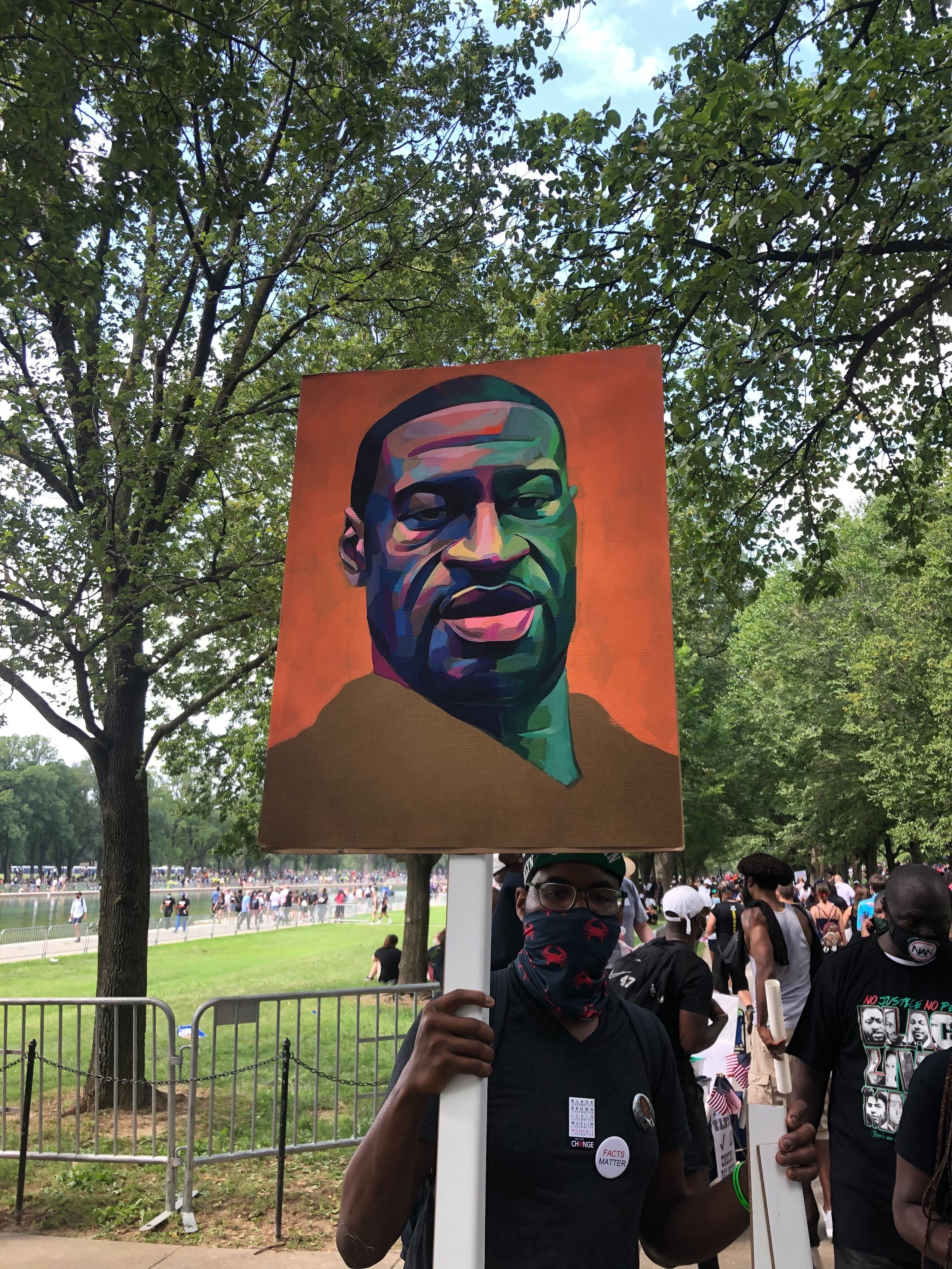 A man holds a large sign with a painting of George Floyd on it