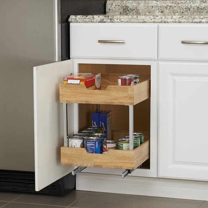 A wood and metal two-tier pull-out drawer holding pantry staples in a kitchen cabinet