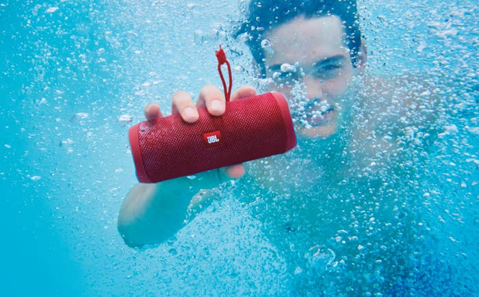 Model holding the cylinder-shaped speaker in red underwater