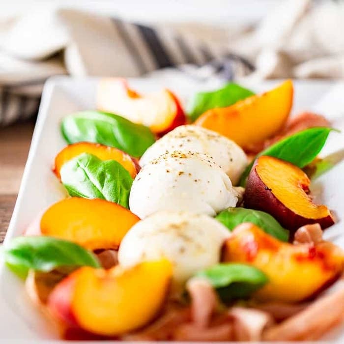 A plate with balls of burrata, sliced peaches, basil leaves, and prosciutto.