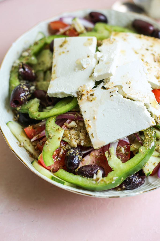 A Greek salad with tomatoes, cucumber, olives, and pepper beneath large chunks of feta cheese.