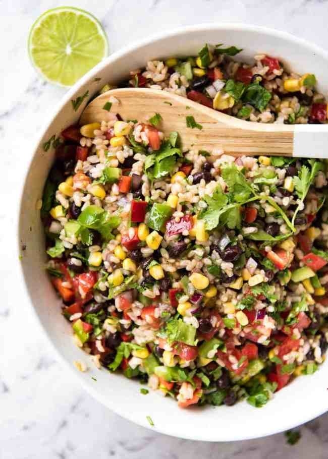A bowl of salad with rice, beans, corn, cilantro, tomatoes, and onion.