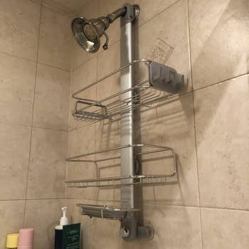 a buzzfeed editor's photo of the stainless steel over-the-shower-head caddy with two shelves and a soap dish holder