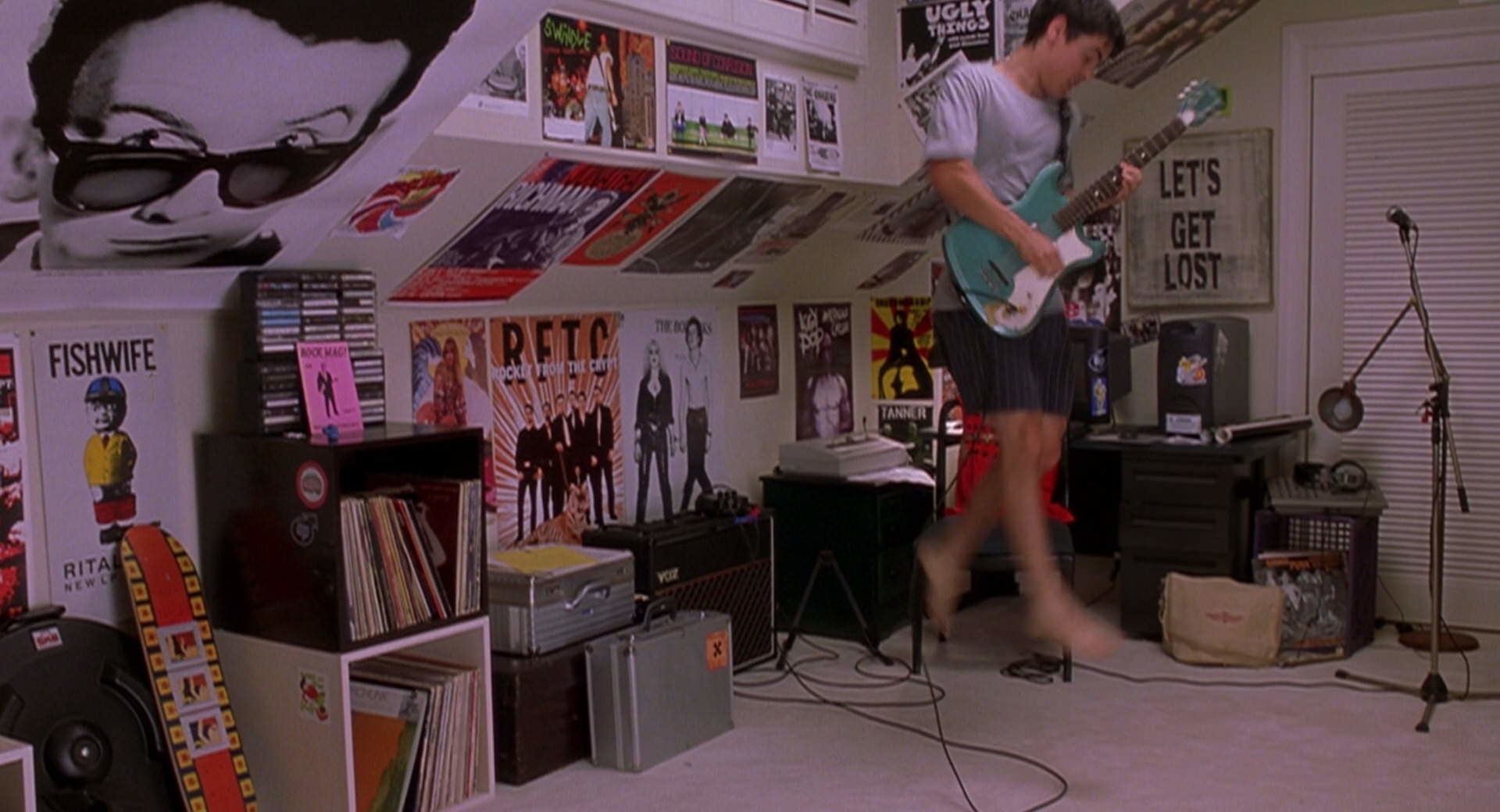 Cliff jumps around his room playing guitar.