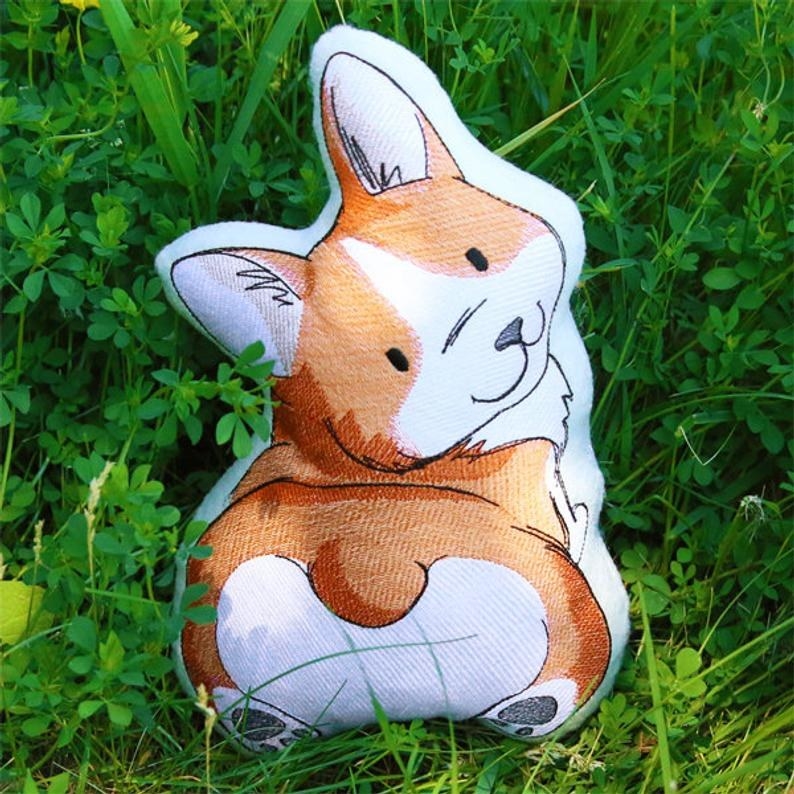 A pillow in the grass of a cartoon looking corgi