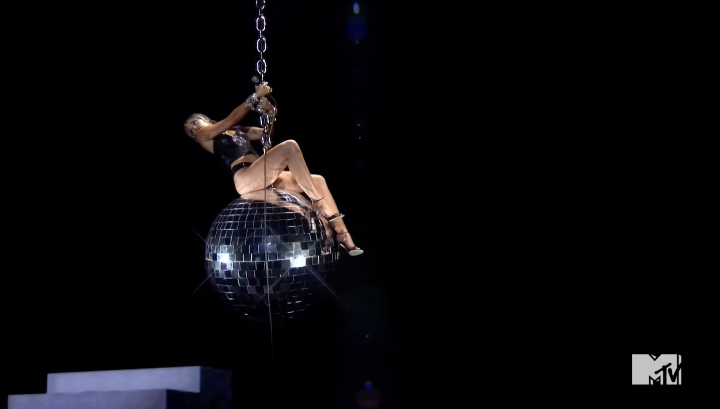 Miley on top of a giant disco ball in the same pose as her original &quot;Wrecking Ball&quot; video