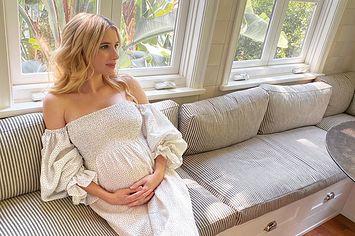 Emma Roberts cradles her baby bump while sitting on the couch