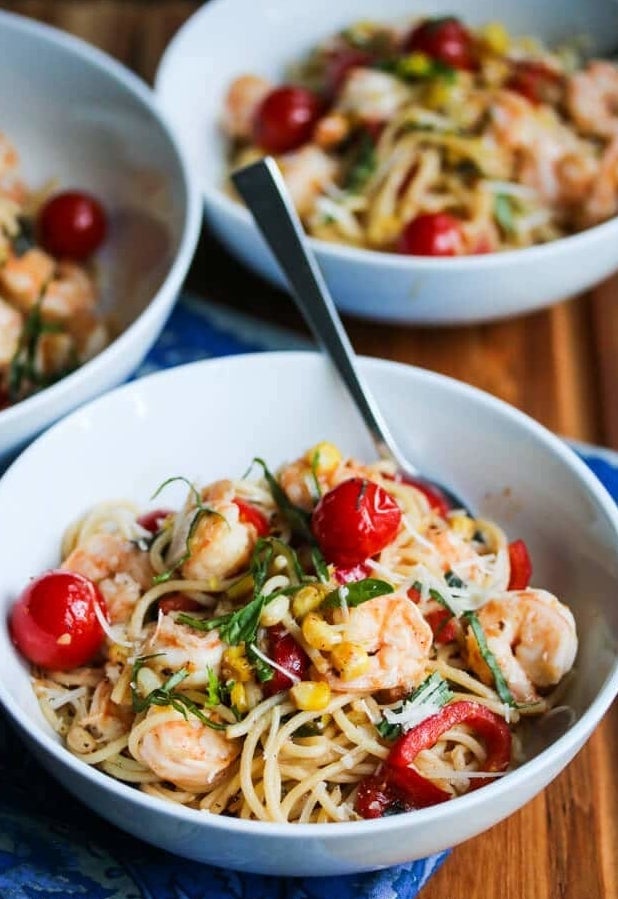 A bowl of spaghetti with corn, cherry tomatoes, shrimp, and torn basil.