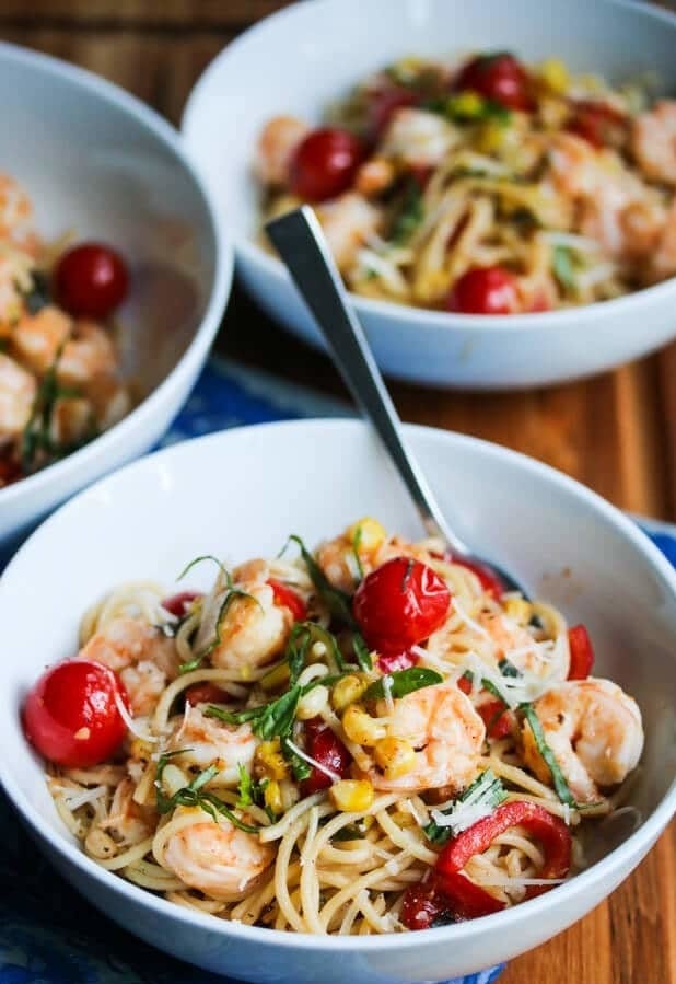 A bowl of spaghetti with corn, cherry tomatoes, shrimp, and torn basil.