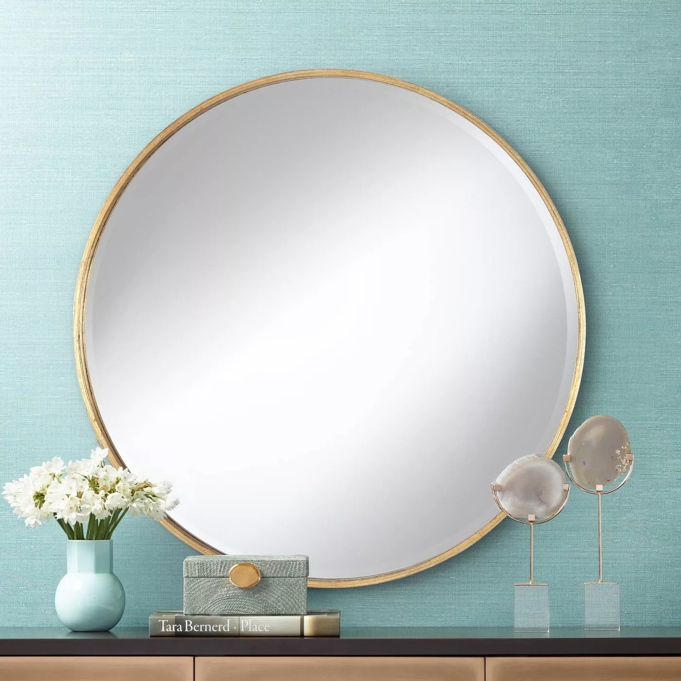 A round mirror with a gold frame mounted on an aqua wall