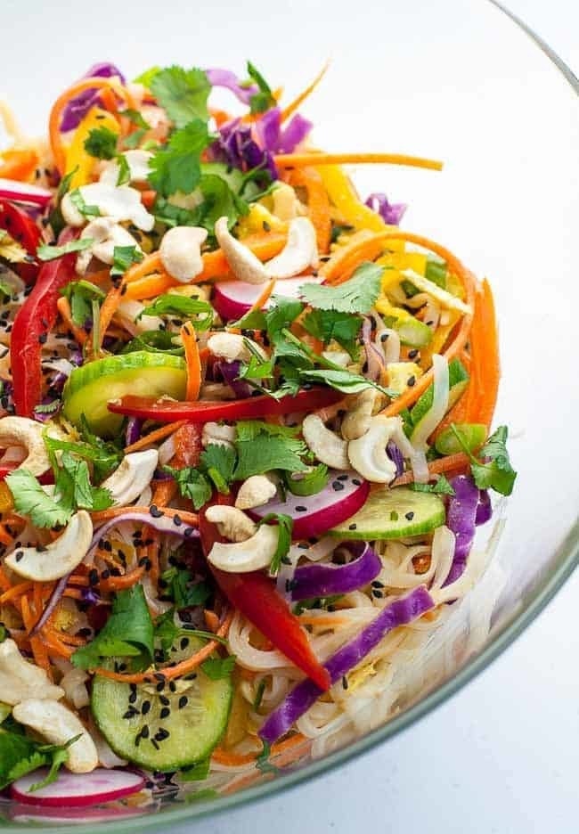 A bowl of rice noodles topped with lots of veggies like cucumbers, radish, cabbage, pepper, carrots, and more.