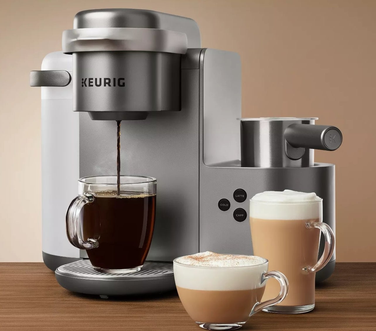 A Keurig making a cup of coffee next to a cappuccino and a latte