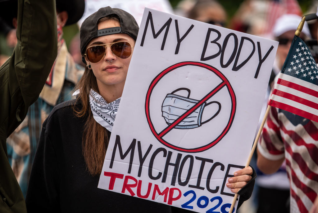 Anti-mask protestor holding a sign that says &quot;my body, my choice&quot; with a red cross over a picture of a face mask
