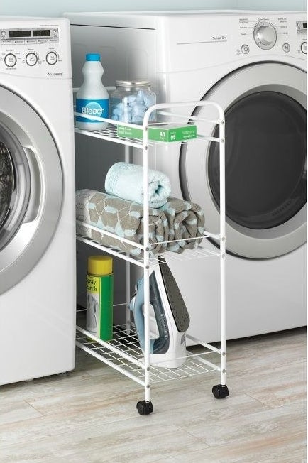 white rolling cart in between a washer and dryer with laundry supplies on it