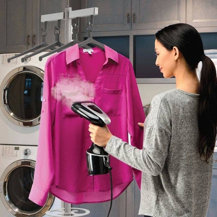 Model using a garment steamer to steam a pink blouse