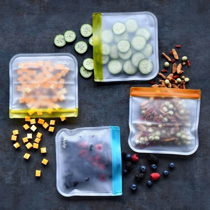 four reusable zipper bags  that are storing cucumber, trail mix, berries, and cheese