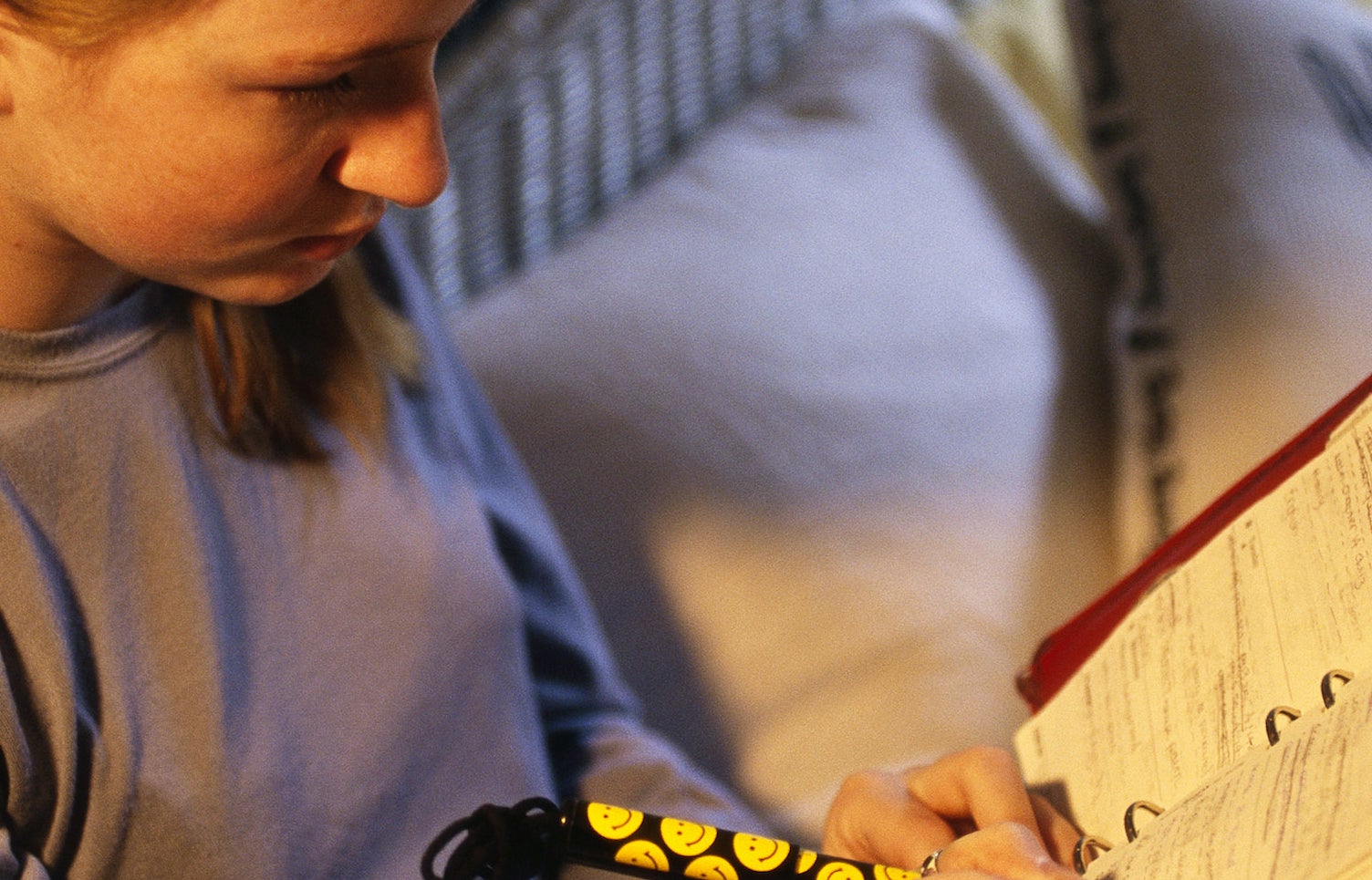 A close-up of a teen age girl writing into her red day planner with a smiley face pen