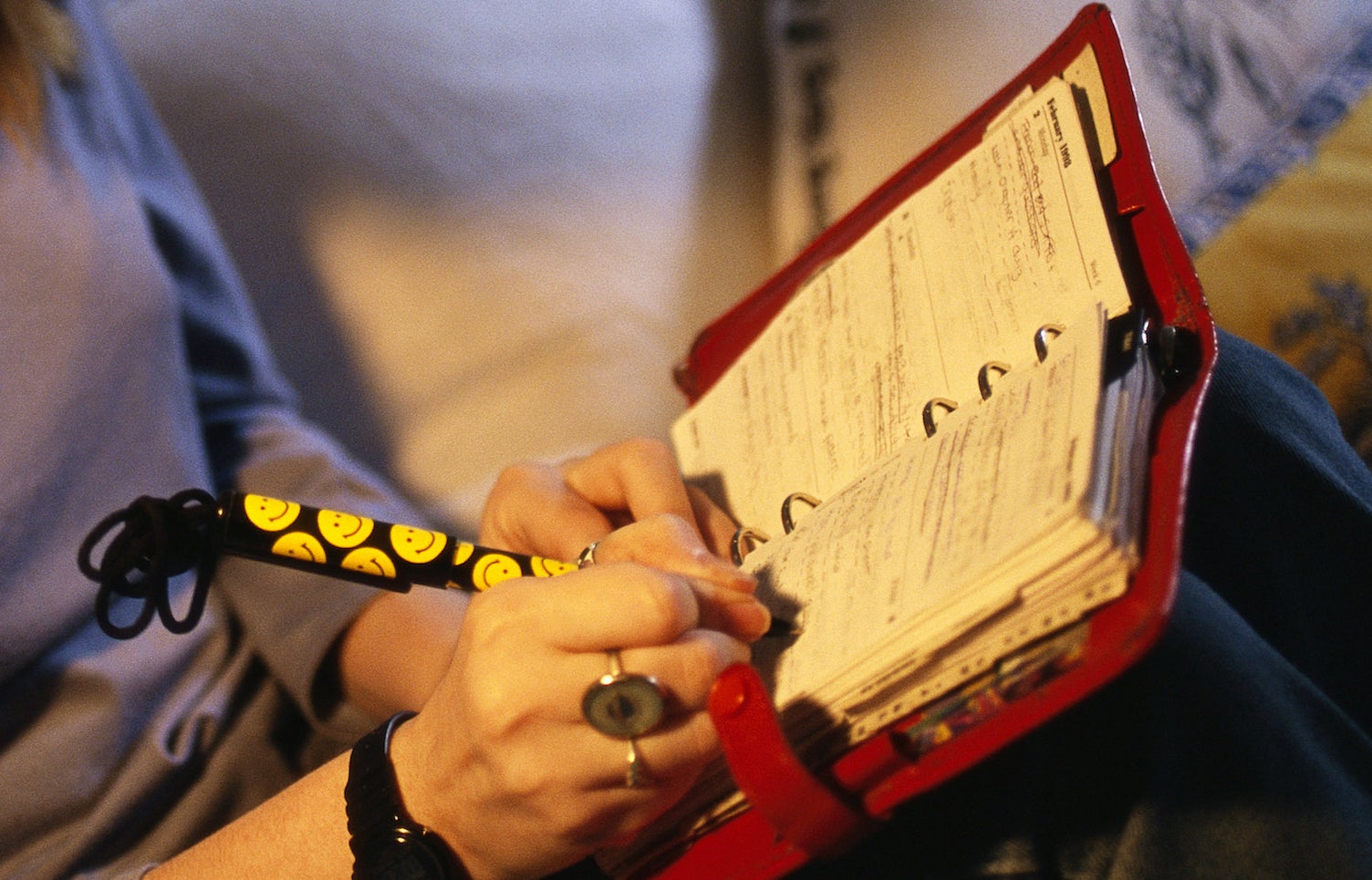 A close-up of a teen age girl writing into her red day planner with a smiley face pen