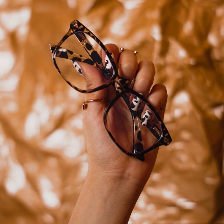 A person holds up a pair of blue light glasses against a graphic background