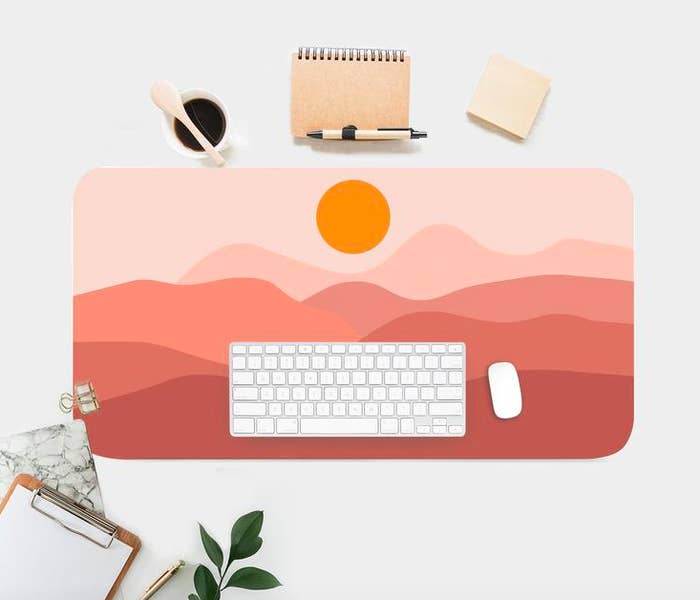 A flatlay of a large desk mat printed with a graphic sunset