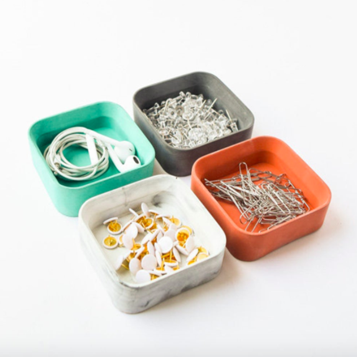 Four cement trays containing small desk accessories, like paper clips and push pins