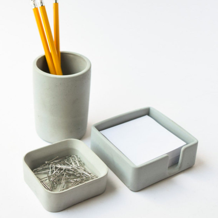 One of the concrete desk trays next to a concrete cup and note pad  
