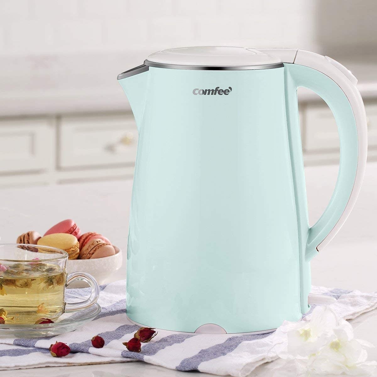 A close up of the kettle next to a cup of tea and a bowl of macarons