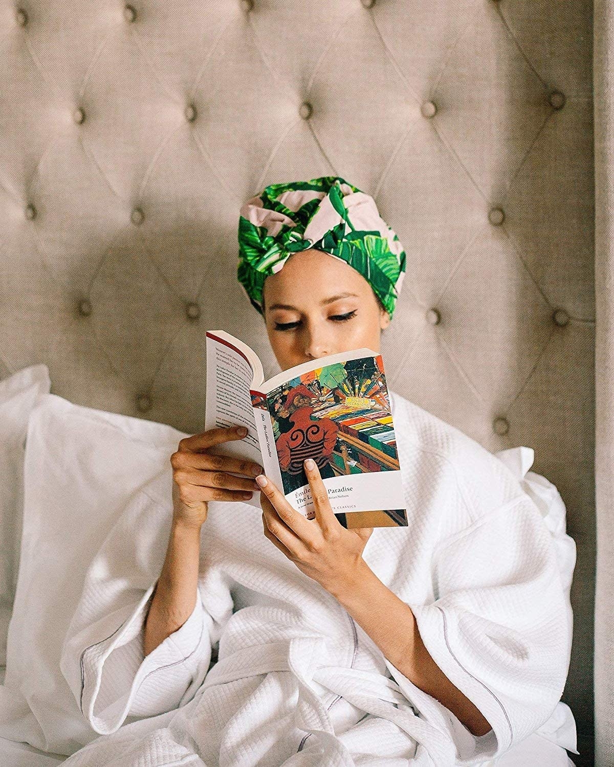 A person reads a book in bed while wearing the tropical print shower cap
