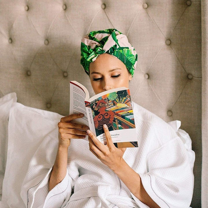 A person reads a book in bed while wearing the tropical print shower cap  