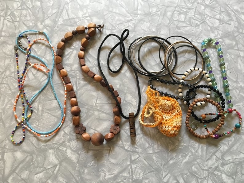 A bunch of different style of necklaces, beads, wood, next to beaded bracelets and silver bracelets 