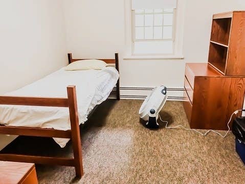 An empty dorm room with one bed, one desk, and a window