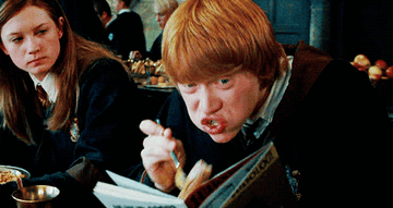 Ron Weasley eating hurriedly while reading 