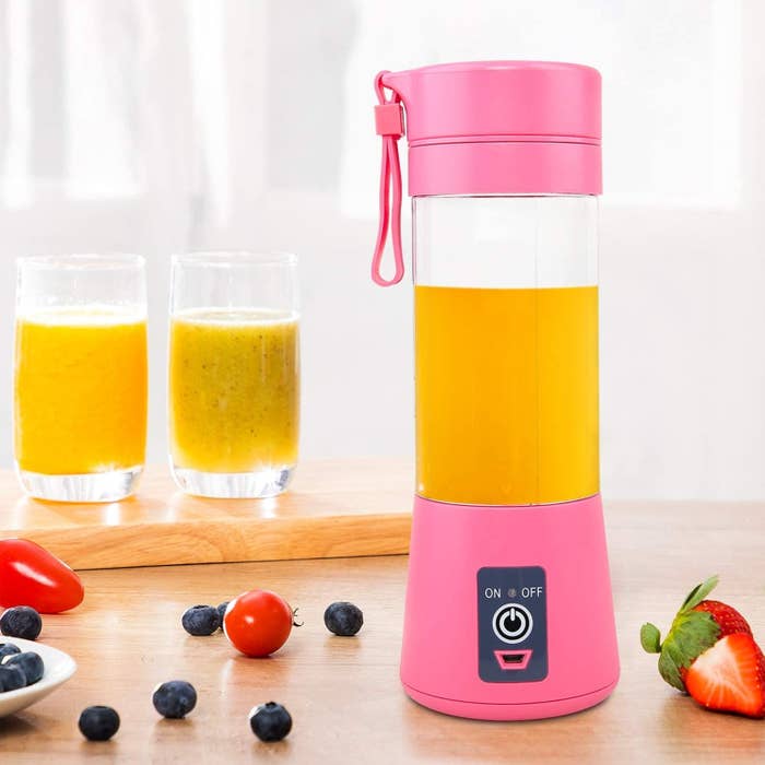 The blender filed with an orange smoothie next to various berries and two glasses filled with smoothies