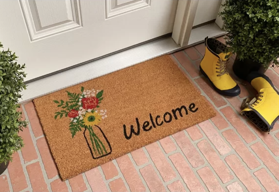 The welcome mat features a colorful vase of flowers on it with the words "welcome" in black