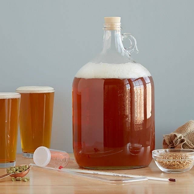 A gallon glass full of beer sits on a table with the rest of the IPA beer brewing kit around it